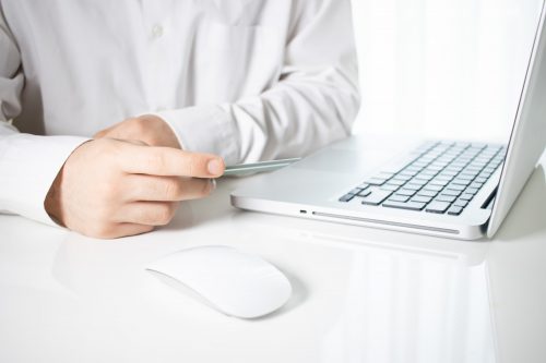 Person Holding A Credit Card With A Laptop And A Computer Mouse On A White Table